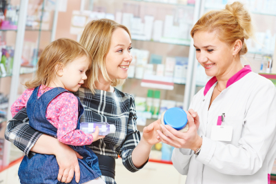 pharmacist woman demonstrating vitamin to child girl with mother in pharmacy drugstore